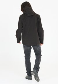 Veste à capuche noire avec des manches longues, fabriquée dans un tissu durable. Coupe décontractée, associée à un jean foncé et des chaussures noires, vue de l'arrière.