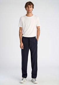 T-shirt blanc à manches courtes et pantalon de jogging bleu marine avec cordon de serrage, associés à des chaussures de sport blanches. Tissu en coton doux, coupe décontractée.