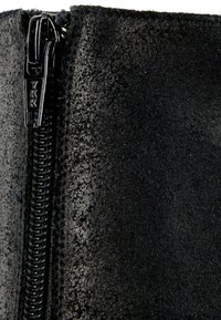 Gros plan d'un tissu texturé noir avec un curseur de fermeture éclair en métal noir marqué "YKK" sur le côté gauche.