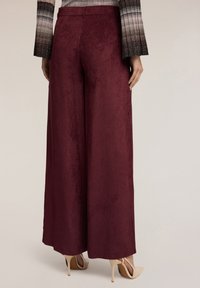 Pantalones de pierna ancha burdeos hechos de un tejido texturizado con un acabado suave, que presentan una cintura de altura media y bolsillos traseros sutiles.
