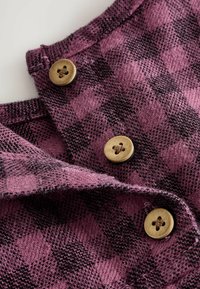 Tissu à carreaux violet et noir avec une texture douce, featuring trois boutons ronds de couleur marron clair. Gros plan sur le détail du col.