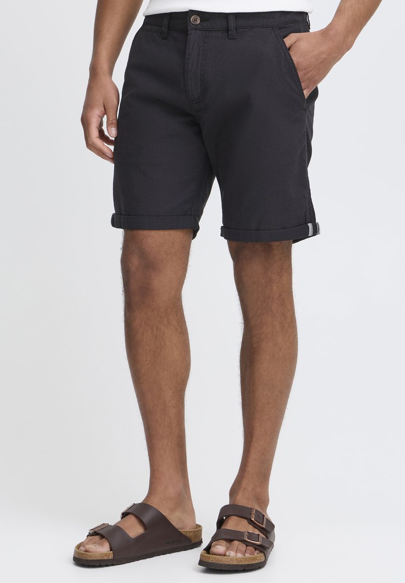 Sorte bomullsshorts med rullekanter, med knappelukking og frontlommer, kombinert med brune sandaler med korksåle.
