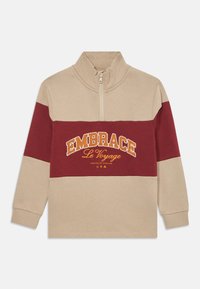 Beige og bordeaux halv-zip sweatshirt med lange ærmer. Har broderet tekst "EMBRACE Le Voyage" i gul. Fremstillet af blødt bomuldsstof.