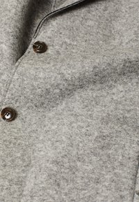 Tejido de mezcla de lana gris con una textura suave, que presenta un botón marrón redondo y un diseño de cuello tradicional.