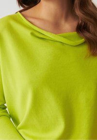Top lungo a maniche con scollatura drappeggiata e off-shoulder di colore verde lime e texture morbida e liscia. Tessuto elastico con dettagli minimi.