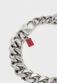 Bracciale in metallo argentato con link spessi, dotato di un'etichetta rossa con il testo "HUGO" e una chiusura robusta.