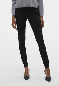 Černé skinny džíny s mírným poškozením, vyrobené z denimu. Kombinované se šedým svetrém a černými botami na podpatku s špičatou špičkou.