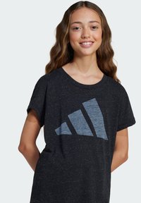 Čierne tričko s krátkym rukávom z textúrovanej tkaniny s veľkým modrým dizajnom loga Adidas. Voľný strih s okrúhlym výstrihom.