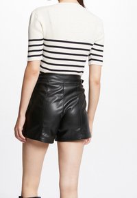 Žebrovaný krémový top s námořnickými pruhy a krátkými rukávy, doplněný o černé vysokým pasem kalhoty z umělé kůže s viditelným švem.