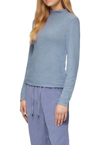 Himmelblaues, langärmliges Oberteil mit hohem Kragen. Hergestellt aus einem weichen, strukturierten Stoff; kombiniert mit passenden, helllila Jogginghosen mit Kordelzug.