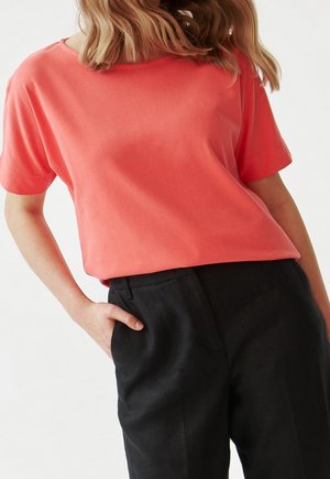 Top corto corallo a maniche corte in tessuto morbido, con vestibilità rilassata e scollo rotondo, abbinato a pantaloni scuri eleganti.