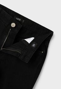 Pantaloni in denim nero con chiusura a zip e bottone. Caratterizzati da una tasca frontale e un'etichetta visibile nell'elastico in vita. Tessuto morbido, materiale resistente.