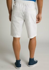 Hvide bomulds shorts med elastisk talje, to baglommer og en ren kant. Båret med blå høje sneakers.