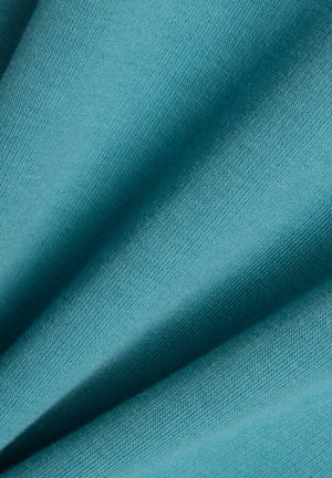 Lähikuva pehmeästä, vaaleansinertävästä kankaasta, jossa on hieno neulepinta ja lempeät laskokset, jotka luovat varjoja ja syvyyttä.