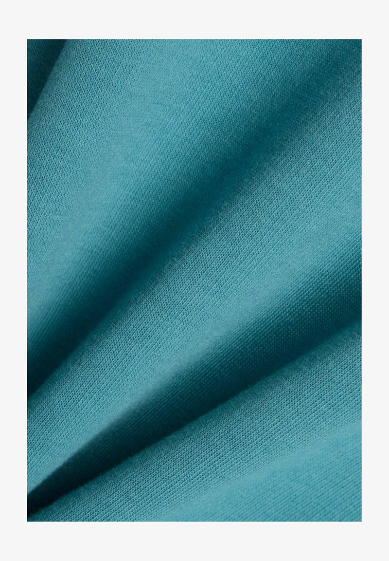 Primo piano di tessuto morbido azzurro chiaro con trama a maglia fine e pieghe delicate che creano ombre e profondità.