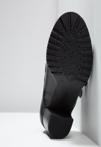 Chaussure en cuir noir avec talon bloc et semelle en caoutchouc texturée, dotée d'une bande de roulement en relief pour une meilleure adhérence et d'un design à bout arrondi.