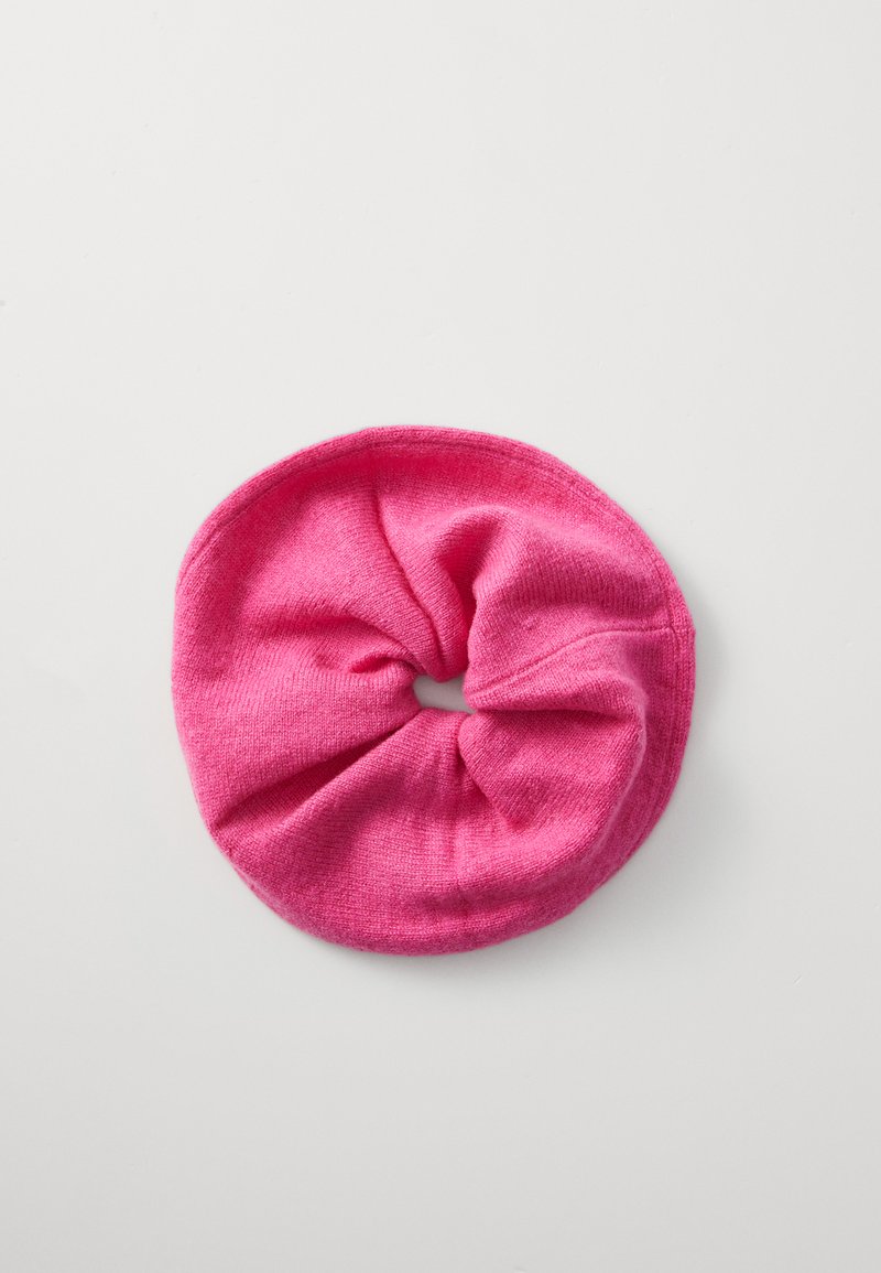 Roze stoffen scrunchie, cirkelvormig, zachte textuur, rekbaar breimateriaal, met een egale kleur en zonder noemenswaardige patronen of hardware.