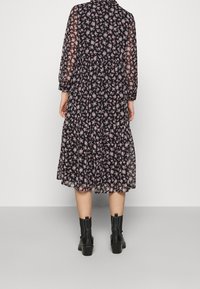 Robe noire à fleurs en tissu transparent, présentant un design à volants, des manches longues et des motifs floraux roses. Associée à des bottines noires.