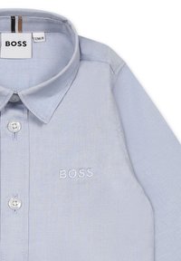 Light blue long-sleeve shirt with a collared neck, embroidered "BOSS" logo in matching color, and a button closure. Smooth fabric texture.