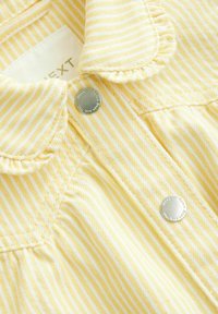 Veste en denim rayée jaune et blanche avec des boutons métalliques ronds et un col, dotée d'une texture douce et de détails de couture.