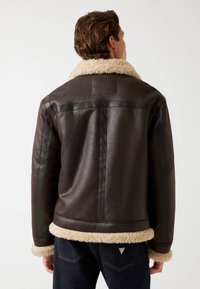 Giacca di pelle marrone con colletto e polsini morbidi beige, caratterizzata da una texture liscia e un design aderente. La giacca presenta cuciture scure a contrasto.