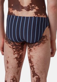 Costumi da bagno navy con strisce verticali azzurro chiaro, caratterizzati da un design senza cuciture e una morbida cintura elastica, indossati da una persona.