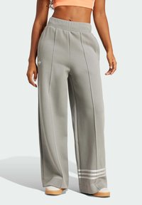 Grå vida sweatpants har en mjuk textur, elastisk midjeband och tre vita ränder som accent vid fållen. Adidas-loggan är synlig.