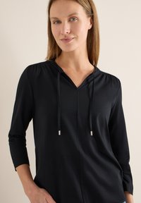 Haut noir à manches longues avec un col en V et des cordons, présentant des fronces aux épaules et une texture lisse et douce.