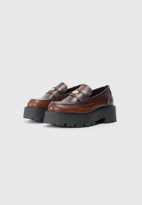 Bruine leren instappers met een chunky zwart plateauzool, voorzien van gouden hardwareaccenten en een gladde afwerking. Gedetailleerde stiksels aan de voorkant.