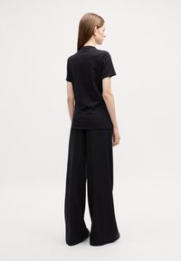 Sort bomulds T-shirt med korte ærmer, rund hals og en slim fit, parret med vide sorte bukser, hvilket skaber et monokromt look.