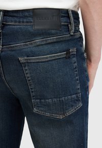 Jeans de mezclilla azul oscuro con una etiqueta de cuero, que cuentan con bolsillos traseros con costuras en contraste y un diseño ajustado.