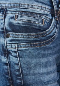 Jeans de mezclilla azul con un diseño clásico de bolsillos, costuras en contraste y una textura suave con ligeros desgastes y detalles de desvanecimiento.