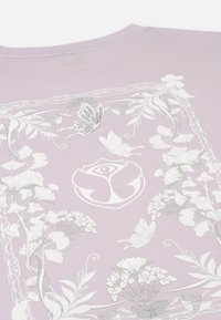 Lila katoen T-shirt met een bloemen- en vlinderontwerp in het wit, omrand door ingewikkelde patronen en een centraal logo-detail.