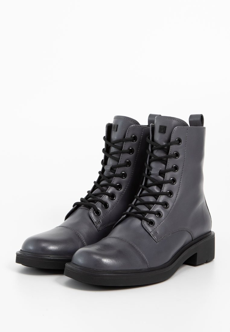 Graue Leder Stiefeletten mit schwarzen Schnürsenkeln, runder Spitze, verstärkten Nähten und einer niedrigen, klobigen Sohle. Mit einer Zuglasche an der Ferse.