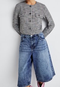 Šedá a vícebarevná kostkovaná zkrácená bunda se dvěma náprsními kapsami, spárovaná s světle modrými džínovými culottes s knoflíkovým zapínáním.