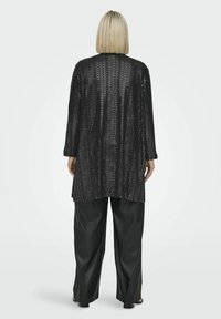 Must-bee kootud must pikem sviiter, millel on tekstureeritud muster, lõdva lõike ja külgmiste lõigetega, kombineeritud laiade mustade nahkpükstega.