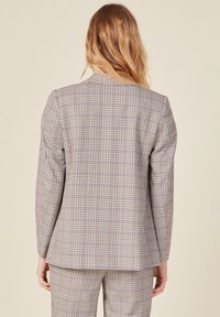 Tarkistettu bleiseri beige, punainen ja sininen sävyissä. Mittatilaustyönä tehty malli rakenteellisilla hartioilla, pitkillä hihoilla ja suoralla helmalla. Kuviollinen rakenne.