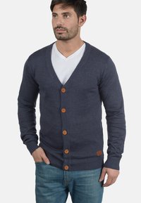 Mörkblå cardigan i stickat tyg, med v-ringning, ribbade manschetter och sex träknappar fram. Avslappnad passform.
