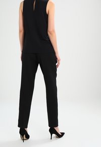 Zwarte mouwloze top met een keyhole-detail aan de achterkant, gecombineerd met op maat gemaakte zwarte broek en zwarte puntige hakken. Glad stofoppervlak.