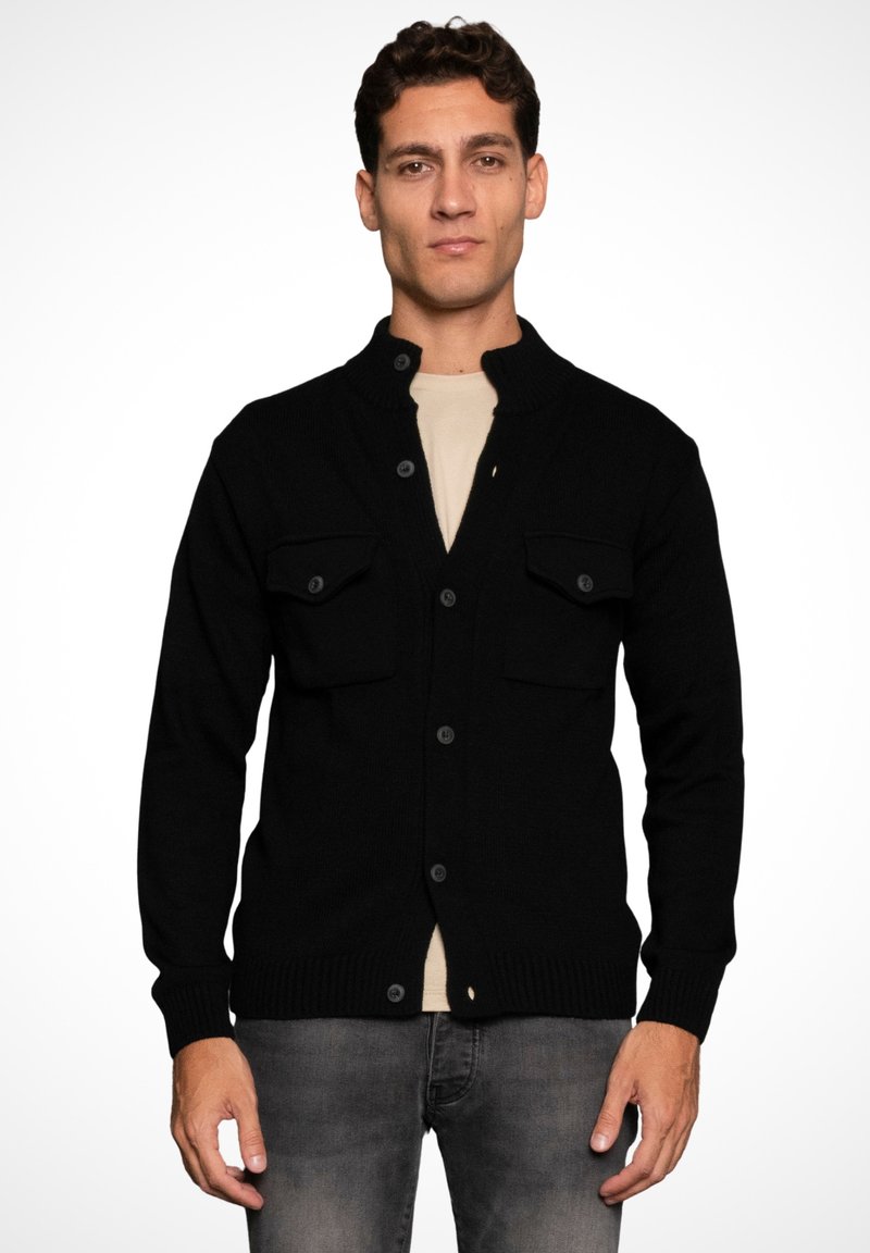 Black knitted cardigan with a high collar, button closure, and two chest pockets. Features ribbed cuffs and hem. Worn over a beige shirt.