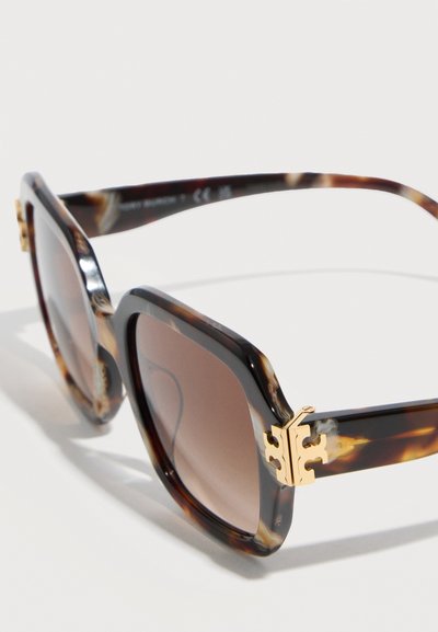 Τετράγωνα γυαλιά ηλίου με φίλτρο διαβαθμισμένου καφέ φακού και χρυσό διακοσμητικό λογότυπο στα πλαϊνά, απεικονιζόμενα σε λευκό φόντο.