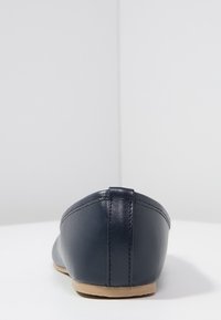 Ballerine in pelle blu navy con retro arrotondato, texture liscia e suola marrone chiaro. Design minimalista senza decorazioni o motivi.
