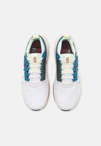 Zapatillas deportivas blancas con acentos en azul y verde, parte superior de malla, textura perforada, lengüeta con patrón y suela clara contrastante.