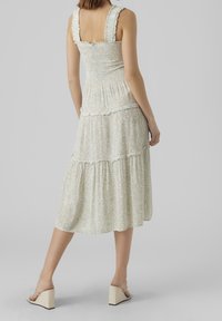 Vaaleanvihreä kukkakuosis midi-mekko, jossa on smokkibodice, kerroksellinen helma ja röyhelöillä varustetut olkaimet. Yhdistetty viistokoroihin kenkiin.