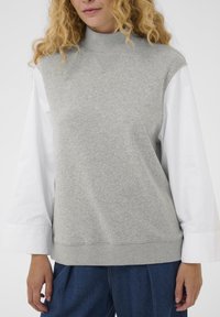 Pull-over gris clair avec un col montant, doté de manches longues blanches. Confectionné en tissu doux avec des textures contrastantes au col et à l'ourlet.