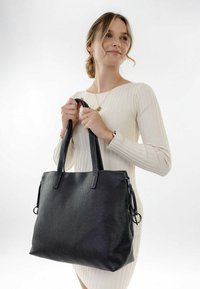 Sac fourre-tout en cuir noir avec une finition texturée, deux poignées et une poche latérale zippée. Design lisse et structuré, dimensions non spécifiées.