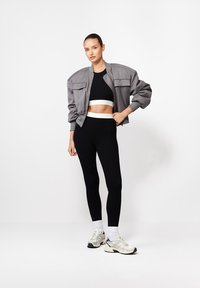 Szara kurtka bombowa na czarnym topie crop, sparowana z czarnymi legginsami i jasnoszarymi butami sportowymi. Gładkie tekstury z dopasowanym krojem.