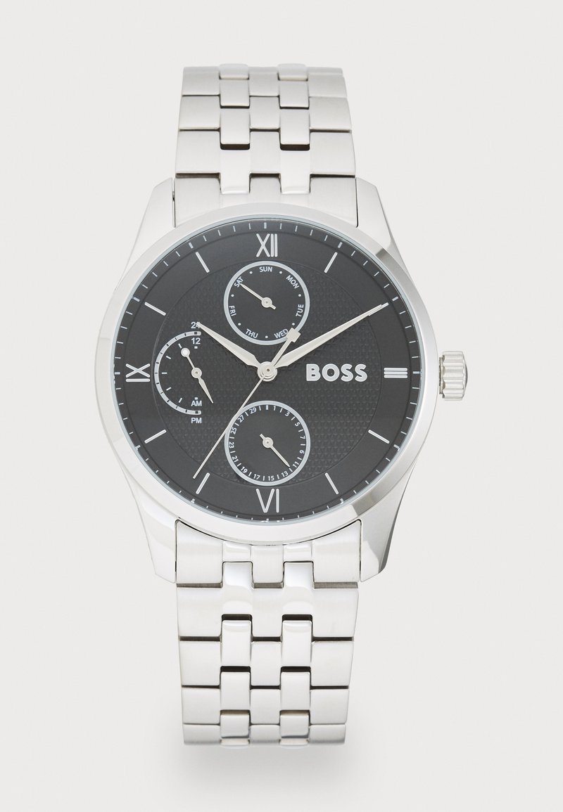 Montre en métal argenté avec un cadran rond noir, aiguilles argentées et chiffres romains. Comprend trois sous-cadrans et un motif texturé.