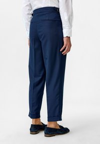 Marineblaue maßgeschneiderte Hose mit entspannter Passform, gefaltetem Saum, Gürtelschlaufen und zwei Gesäßtaschen. Glatte Stoffoberfläche.