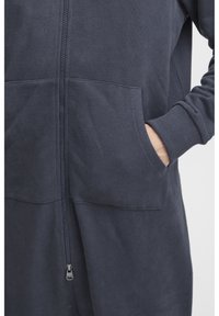 Tamno plavi zip-up dukserica od mekanog pamučnog materijala s velikim prednjim džepovima, rebrastim manžetama i glatkim zatvaračem.